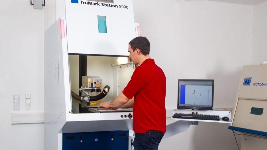 Laserbeschriftung mit TruMark 5000 – SLT – Edwin Schmitt Lasertechnik Ein Mitarbeiter von Edwin Schmitt Lasertechnik arbeitet an der TruMark Station 5000 zur präzisen Laserbeschriftung von Metallbauteilen.