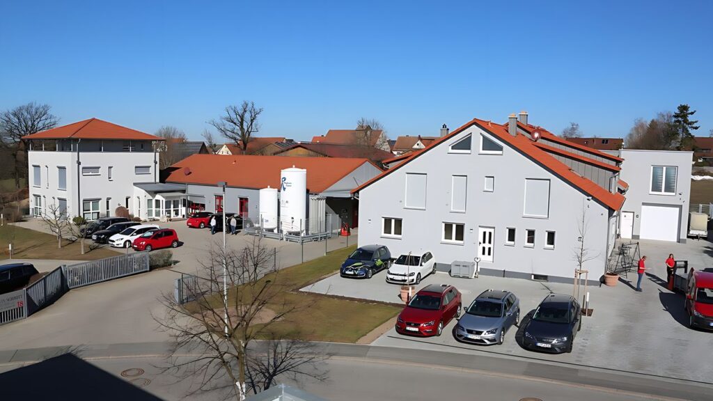 Firmensitz Edwin Schmitt Lasertechnik – Edwin Schmitt Lasertechnik Moderne Firmengebäude der Edwin Schmitt – Lasertechnik GmbH in Kalchreuth mit Parkplätzen und Produktionshallen bei sonnigem Wetter.